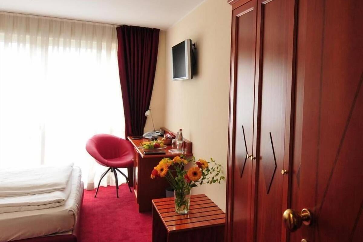 Ett hotellrum med en säng, ett skrivbord med en dator, en stol, ett litet bord med en vas med blommor och en garderob.