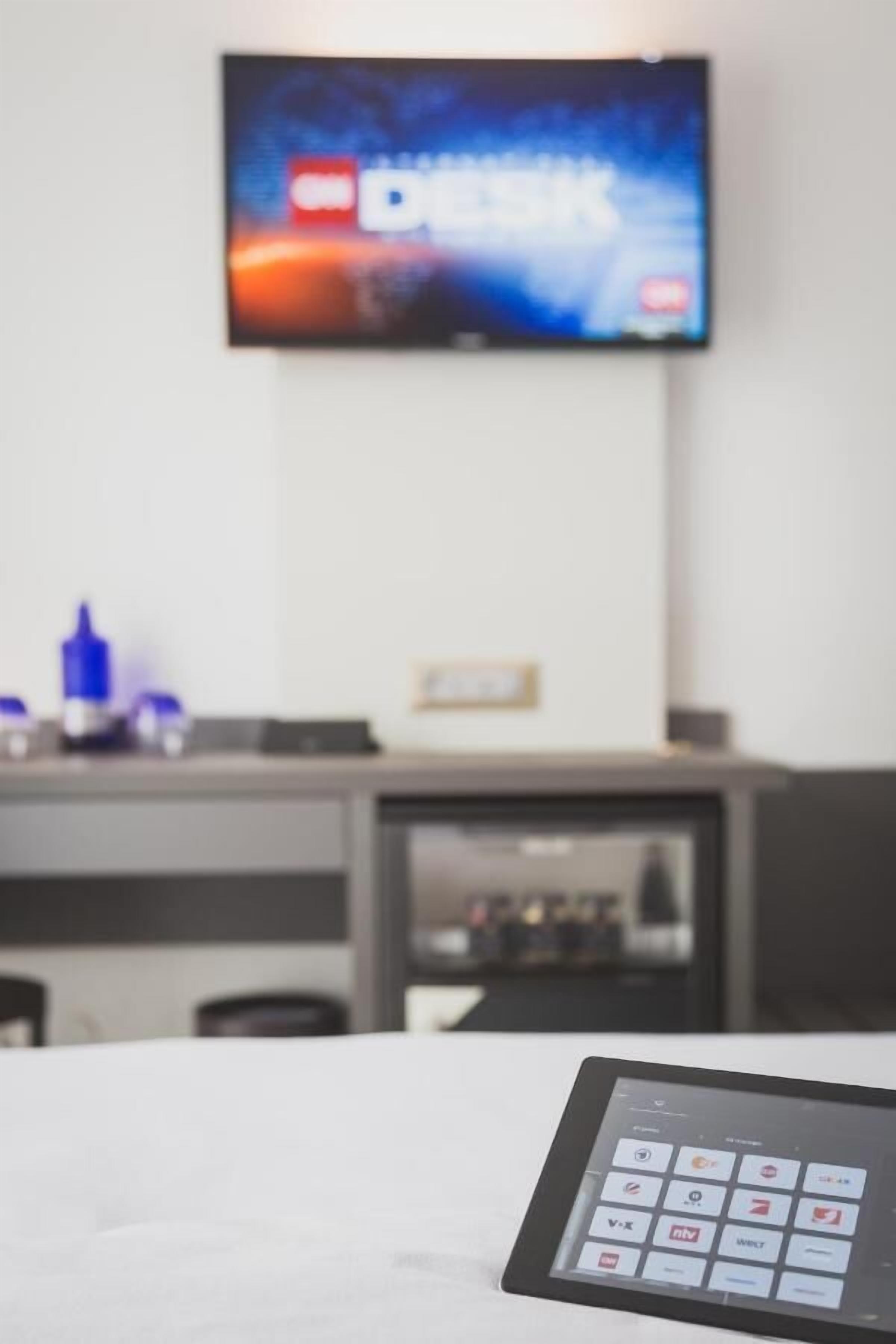Un hall d’hôtel avec un téléviseur fixé au mur diffusant une chaîne d’information, un comptoir d’accueil et, au premier plan, un lecteur de cartes-clés numériques.