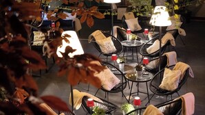 Un espace extérieur aménagé avec des tables rondes et des chaises en fil de fer noir, entouré du feuillage automnal.