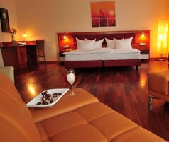 Una habitación de hotel con una cama grande, una mesita de noche con una lámpara, una pequeña mesa con un plato de bombones y una copa de postre.