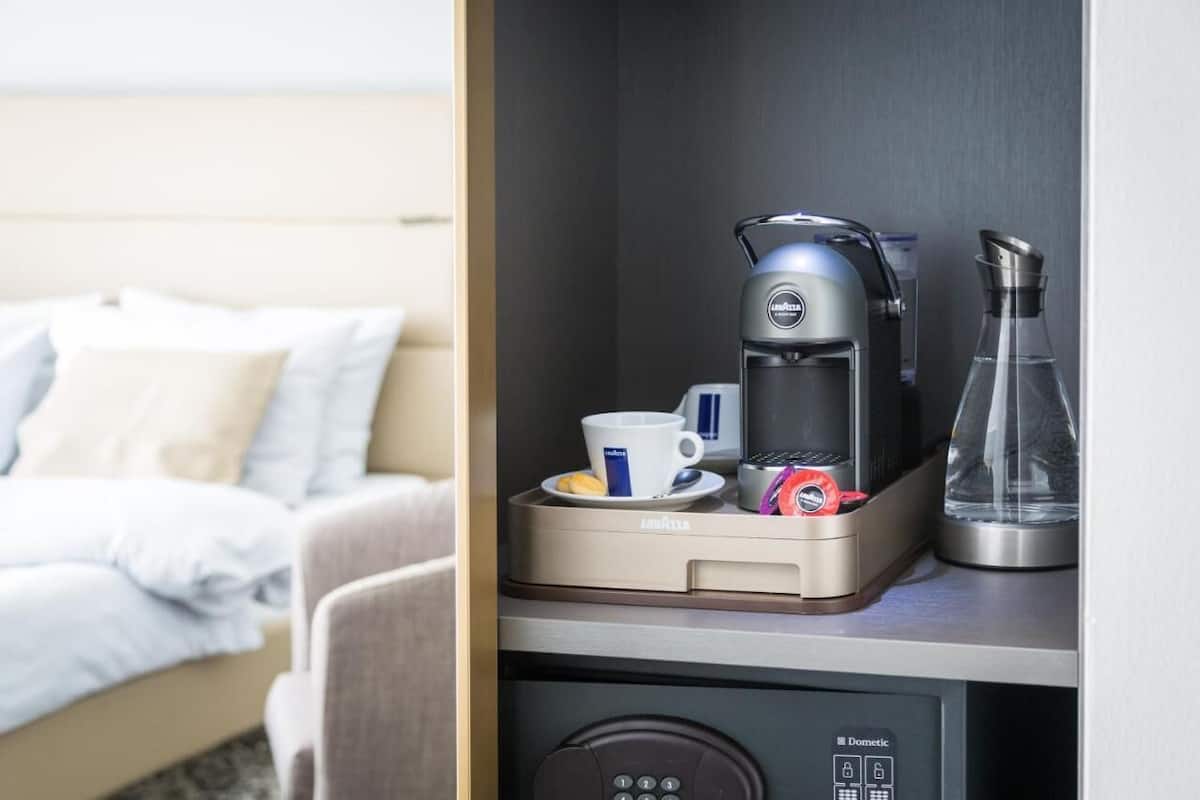 Ett hotellrum med en säng, en kaffebryggare, en kopp och en glaskanna på en bänk.