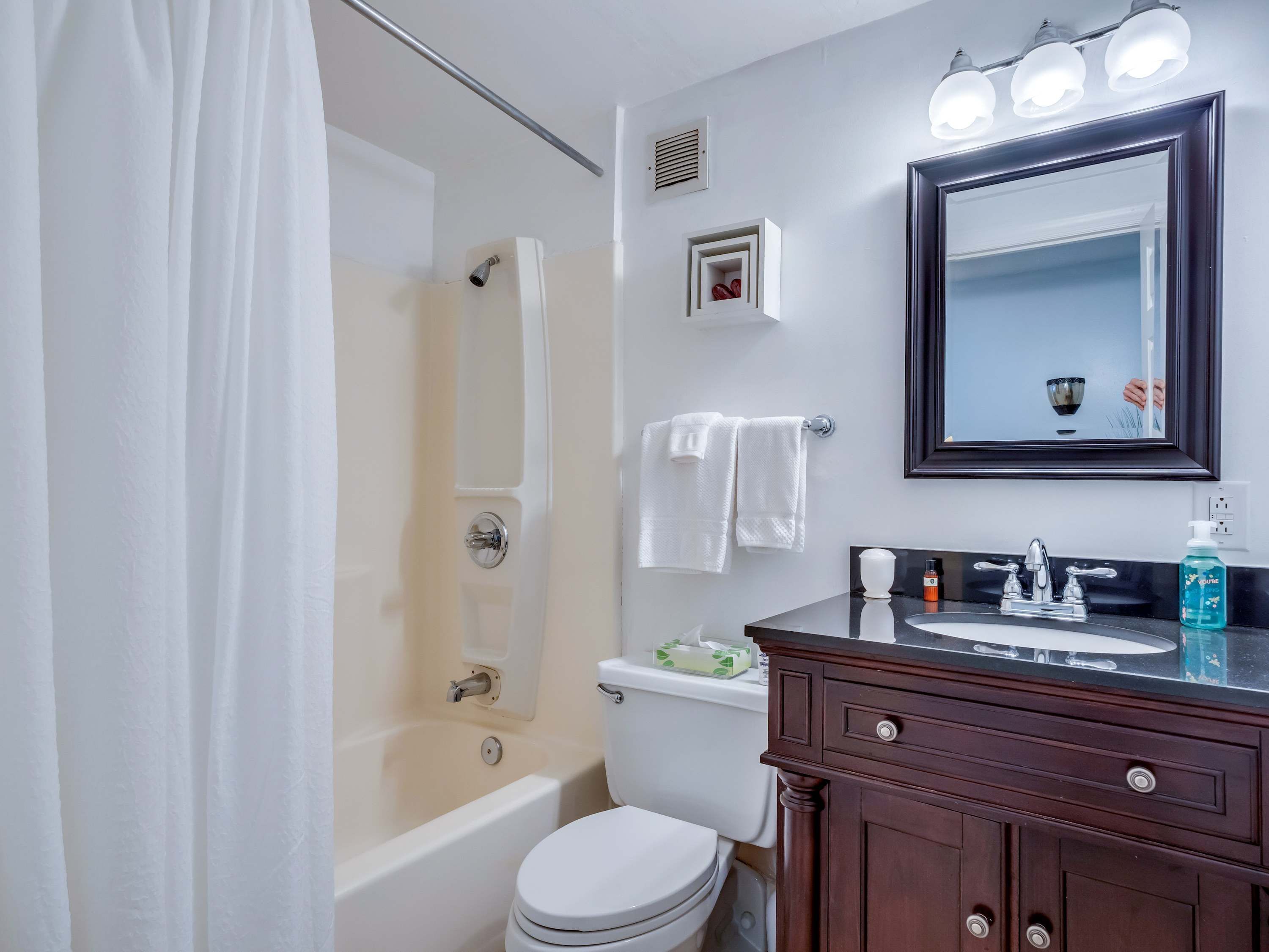 A bathroom with a bathtub, toilet, and vanity with a mirror and lights.