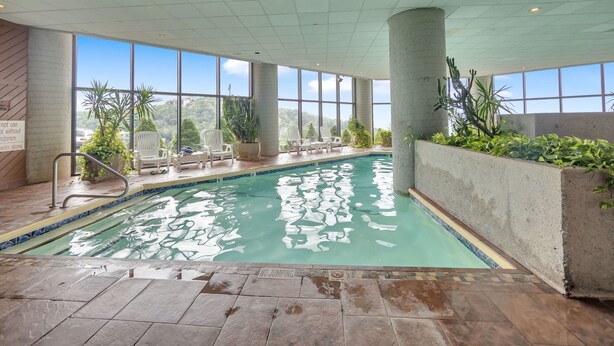 Una piscina interior con vistas claras del paisaje circundante, rodeada de plantas en macetas y sillas blancas.
