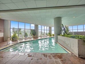 En inomhuspool med fri utsikt över det omgivande landskapet, omgiven av planterade växter och vita stolar.
