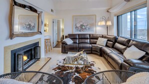 Una sala de estar moderna con chimenea, sofá de cuero, mesa de centro de vidrio y obras de arte en las paredes.