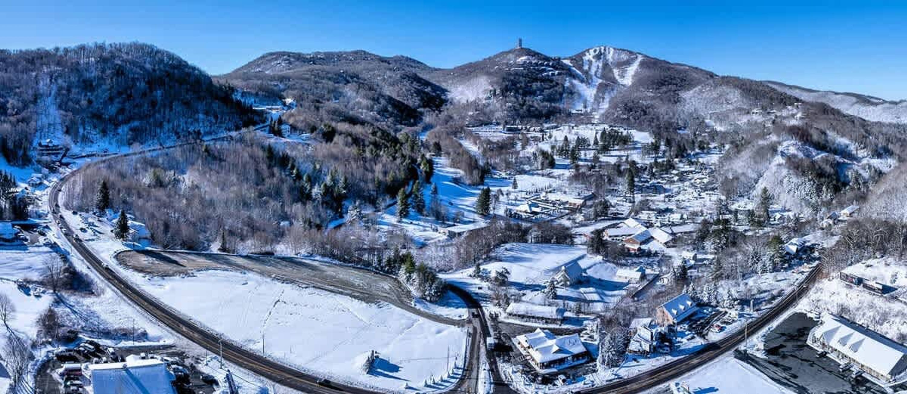 A winter landscape with a snow-covered town, a railway track, and a mountain in the background.