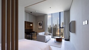 Une chambre d’hôtel moderne dotée d’un grand lit, d’un canapé, d’un bureau et offrant une vue sur le paysage urbain.