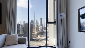 Une chambre d’hôtel moderne dotée d’une grande porte-fenêtre coulissante donnant sur la ville, d’un canapé, d’une table ronde et d’un lampadaire.