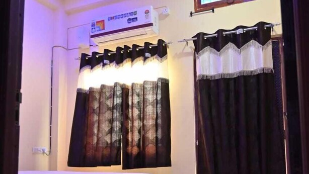 A bedroom with a bed, an air conditioning unit, a window with curtains, and a ceiling fan.