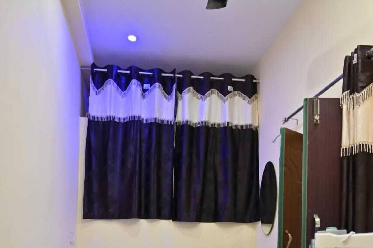 Ein Schlafzimmer mit einem Einzelbett, einem Fenster mit Vorhängen, einer Tür und einer Heizung.