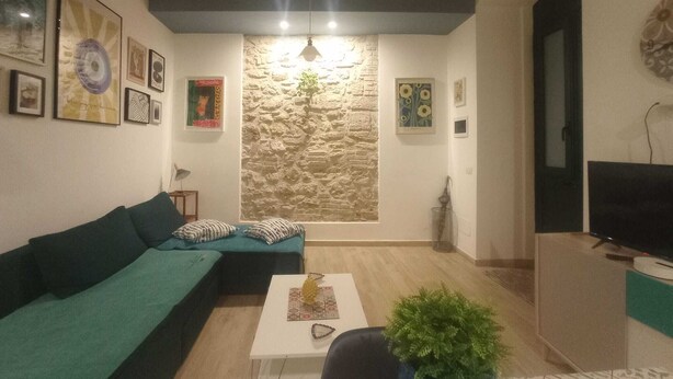 A cozy living room with a stone wall, a green sofa, a small table, and a TV. - Palermhost (Palermo)