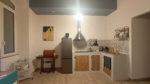 A compact kitchen with a refrigerator, wooden cabinets, a dining table, and a hanging light fixture. - Palermhost (Palermo)