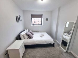 Quarto com cama, mesa de cabeceira, janela e espelho.