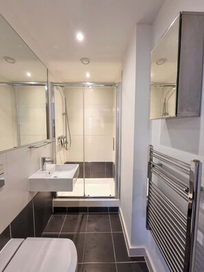 Uma casa de banho moderna com cabine de duche em vidro, lavatório branco e sanita integrada.