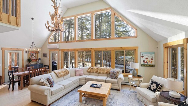A spacious living room with a large sectional sofa, a wooden coffee table, and a chandelier. - Family Retreat | 10 Min to Okemo (Ludlow)