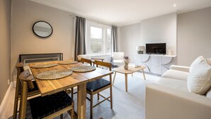 A modern living room with a wooden dining table, white sofa, and a TV. - Stylish Flat, short walk to town (Oxford)