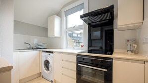A modern kitchen with a washing machine, oven, and a window providing natural light. - Stylish Flat, short walk to town (Oxford)