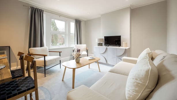 A modern living room with a sofa, chairs, a coffee table, a TV, and a window with curtains. - Stylish Flat, short walk to town (Oxford)