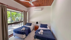 A room with two beds, a ceiling fan, a nightstand, and a window with curtains.