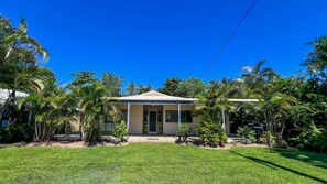 A single-story house with a front porch, surrounded by a well-maintained lawn and tropical vegetation. - Bluefin House beachfront access (Mission Beach)