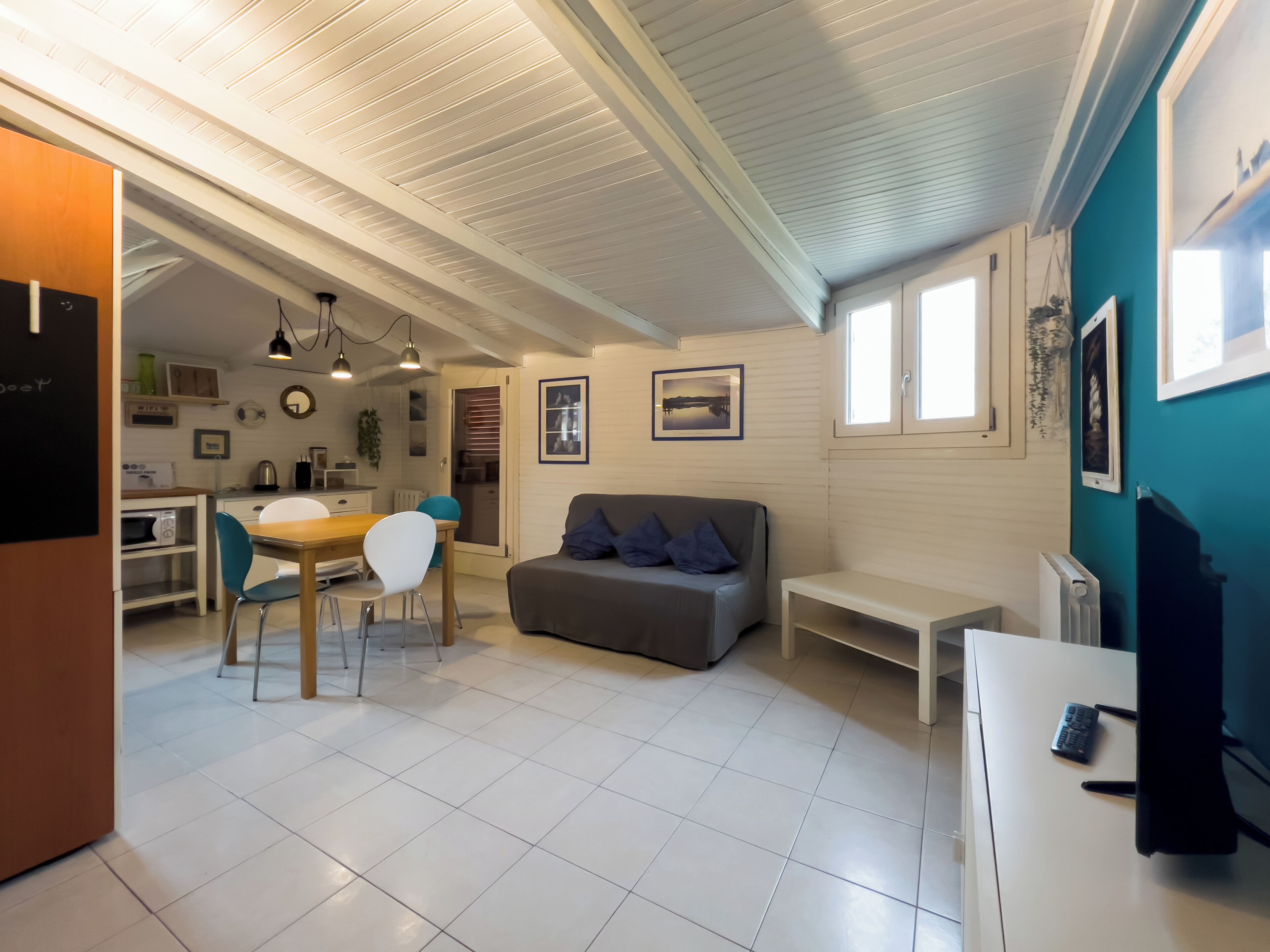 A compact living space with a dining area, a sofa, a TV, and a kitchen in the background.