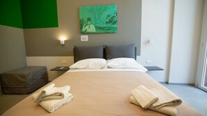 Et hotelværelse med seng, puder, et natbord, et ophængt billede og et vindue.