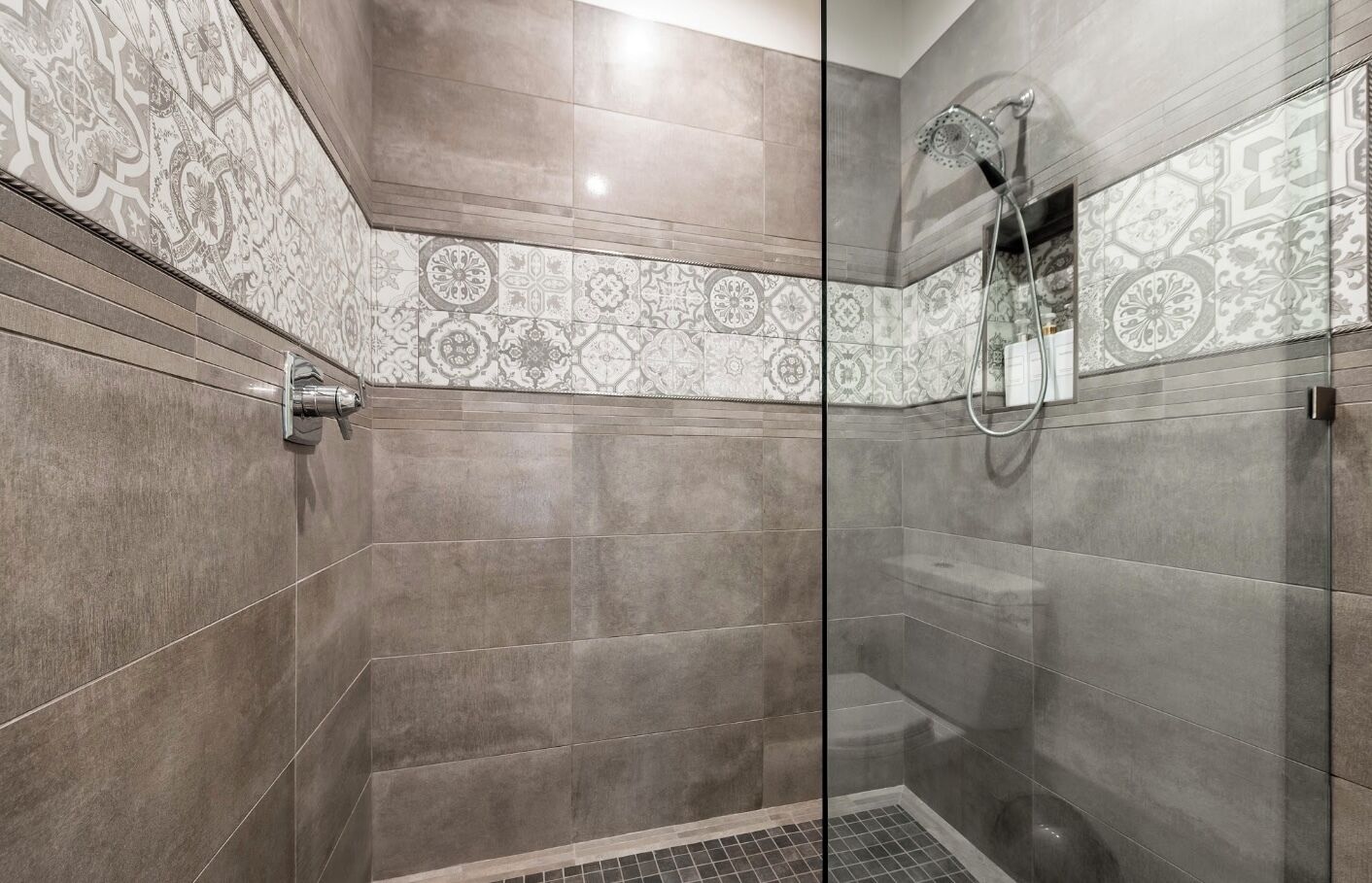 A modern shower with a glass door, patterned tiles, and a handheld showerhead.