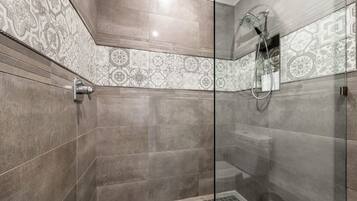A modern shower with a glass door, patterned tiles, and a handheld showerhead.