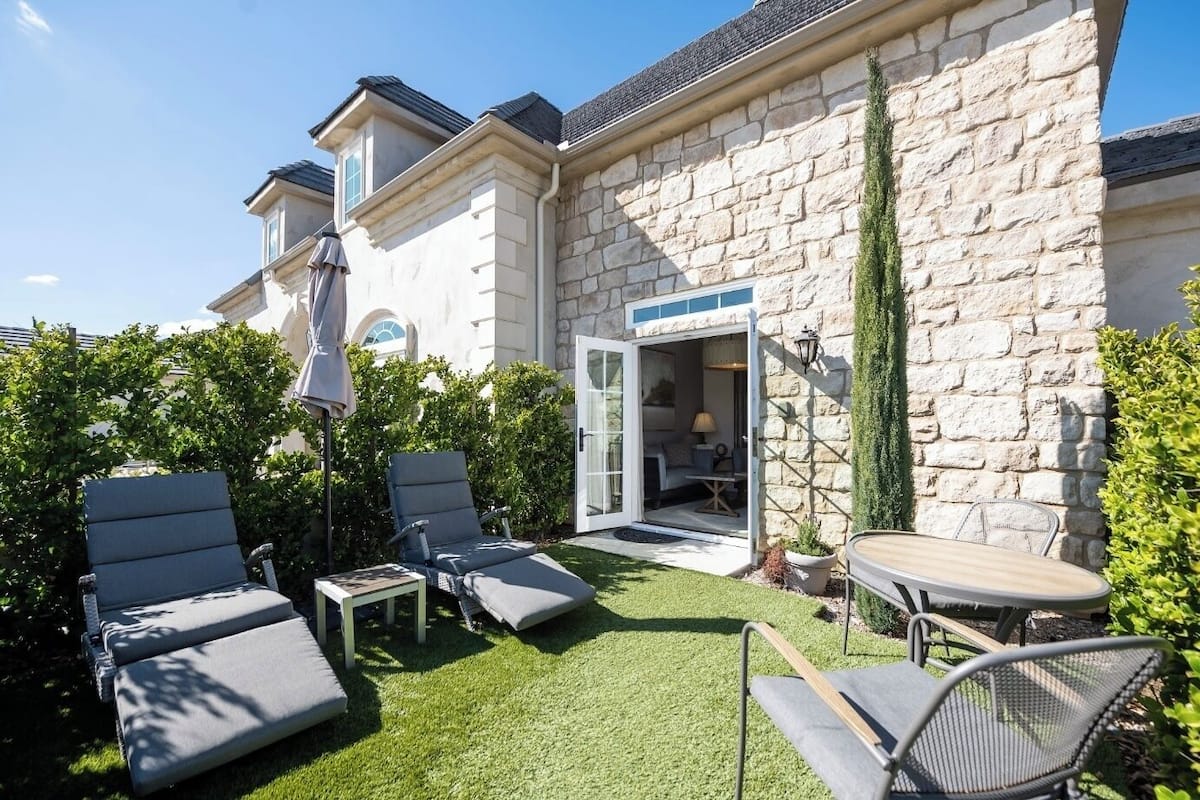 Une maison en pierre dotée d’un patio comprenant des chaises longues, une table et une porte donnant sur un espace intérieur.