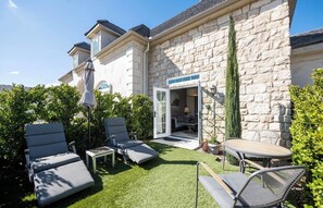 A stone house with a patio area featuring lounge chairs, a table, and a door leading to an interior space. - Domaine Chardonnay (Temecula)