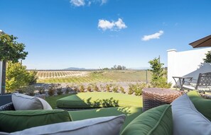 A patio with outdoor furniture, a view of a vineyard, and a clear sky. - Domaine Chardonnay (Temecula)