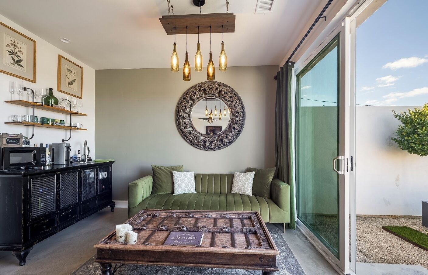 A modern bedroom with a green sofa, a wooden coffee table, a decorative mirror, and a sliding glass door to the outside.