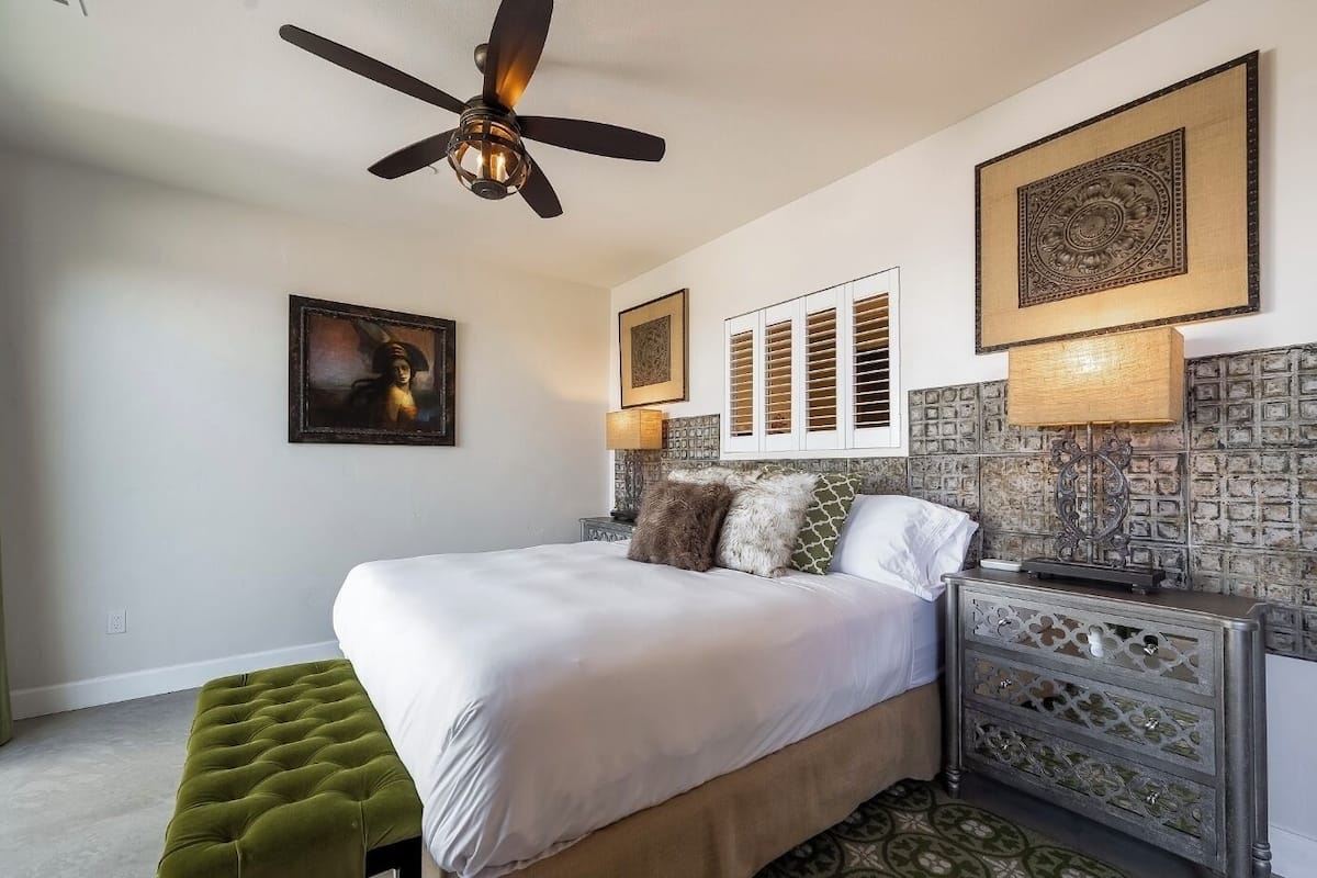 Une chambre à coucher comprenant un lit, un pouf vert, un ventilateur de plafond et des panneaux décoratifs sur les murs.