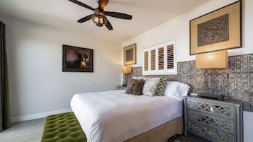 A bedroom with a bed, a green ottoman, a ceiling fan, and decorative wall panels.