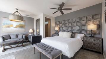 Een moderne slaapkamer met een groot bed, een plafondventilator, een decoratief wandpaneel en een zithoek met een bank en een bijzettafeltje.