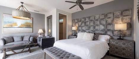 Une chambre moderne avec un grand lit, un ventilateur de plafond, un panneau décoratif mural et un coin salon comprenant un canapé et une table basse.