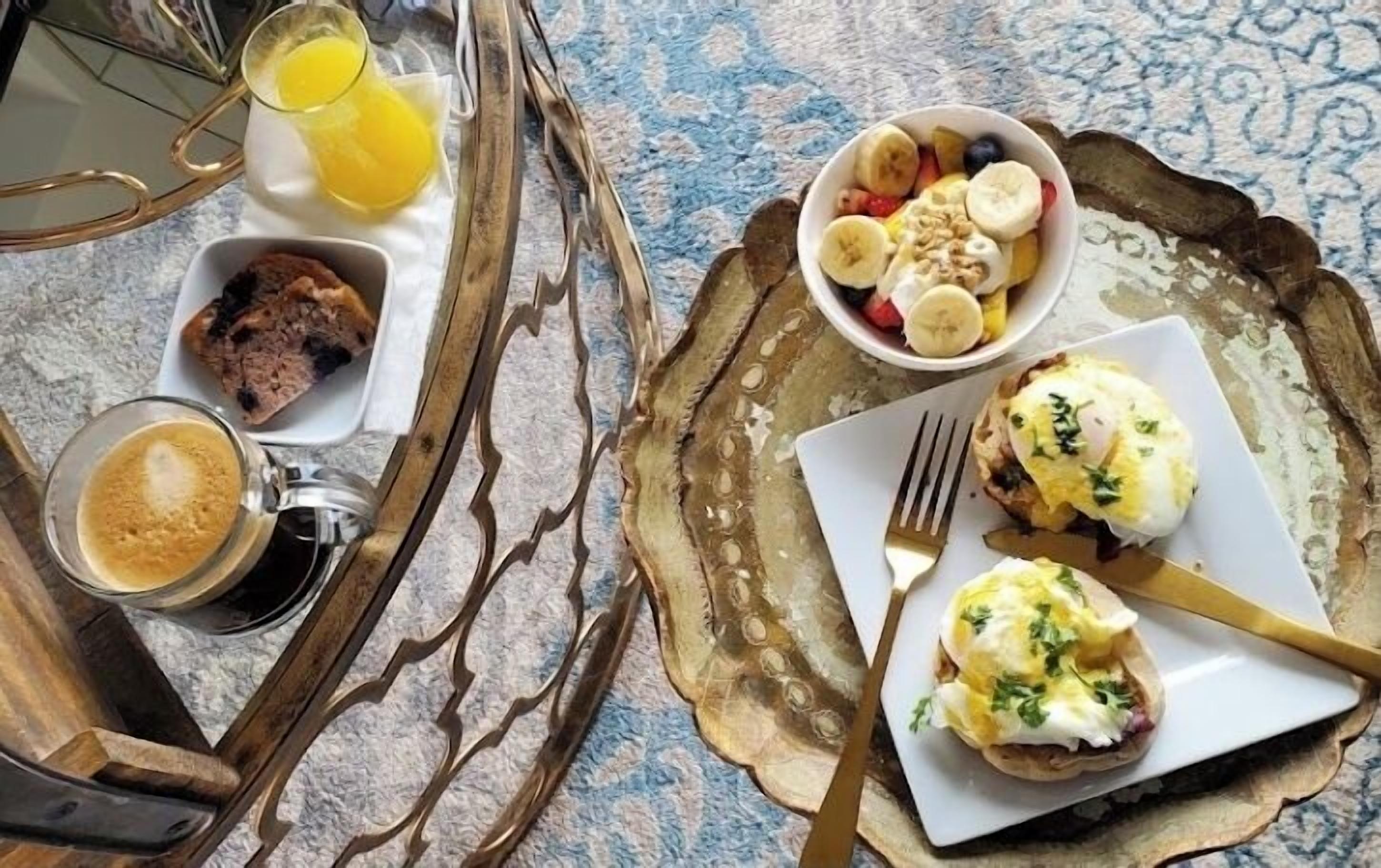 A breakfast tray with eggs benedict, a bowl of fruit, and a glass of orange juice.