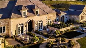 A large stone house with a well-maintained garden, a fountain, and a vineyard in the background. - Domaine Chardonnay (Temecula)