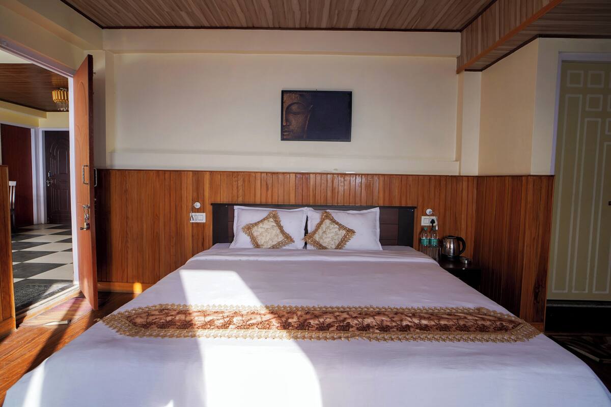 Een opgemaakt bed met een bedsprei met patroon, een houten hoofdbord en een aan de muur bevestigd schilderij.