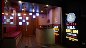 Un'area reception di un hotel con una scrivania, posti a sedere e diverse televisioni a parete.