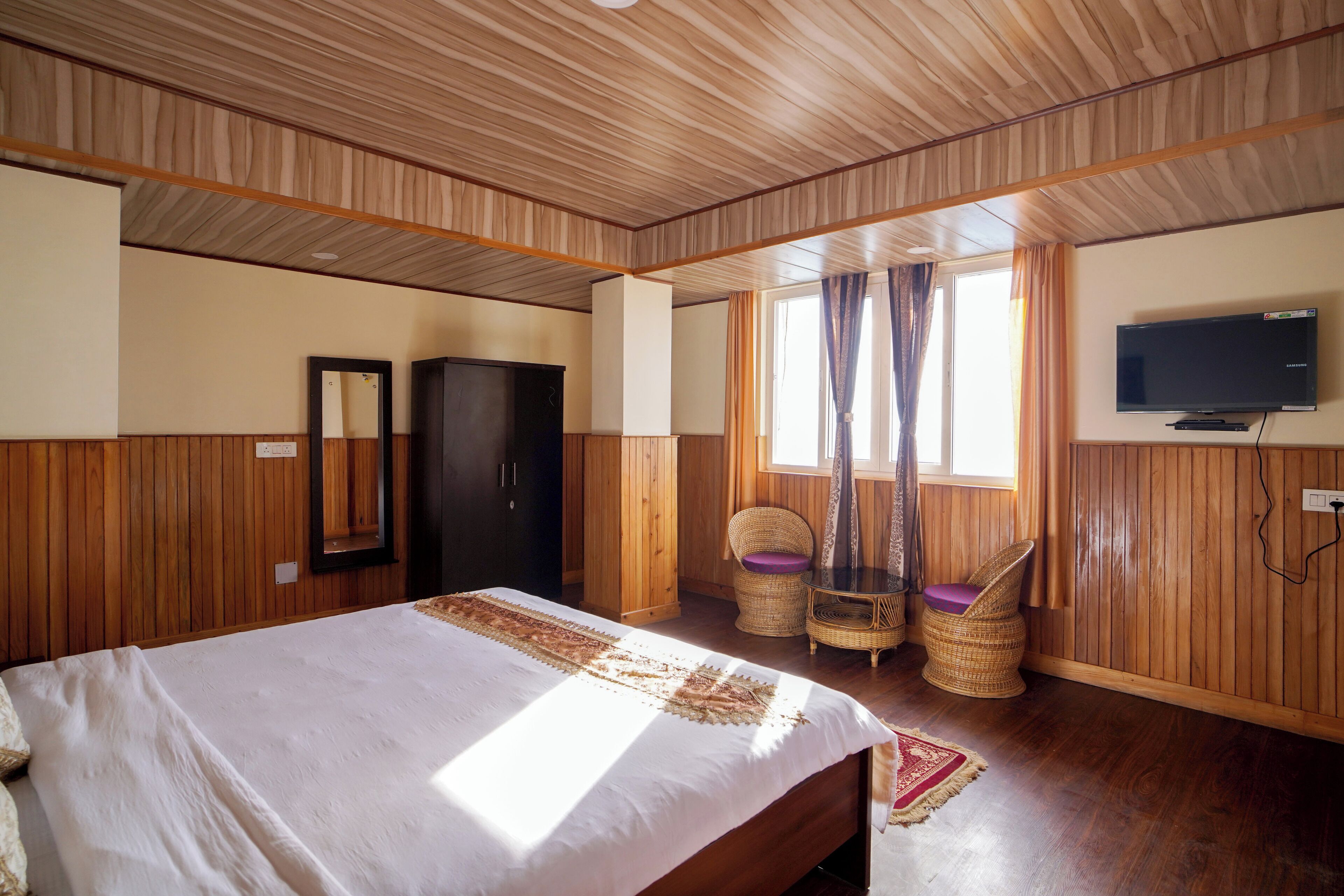 A room with a bed, a television, a wardrobe, and two wicker chairs.