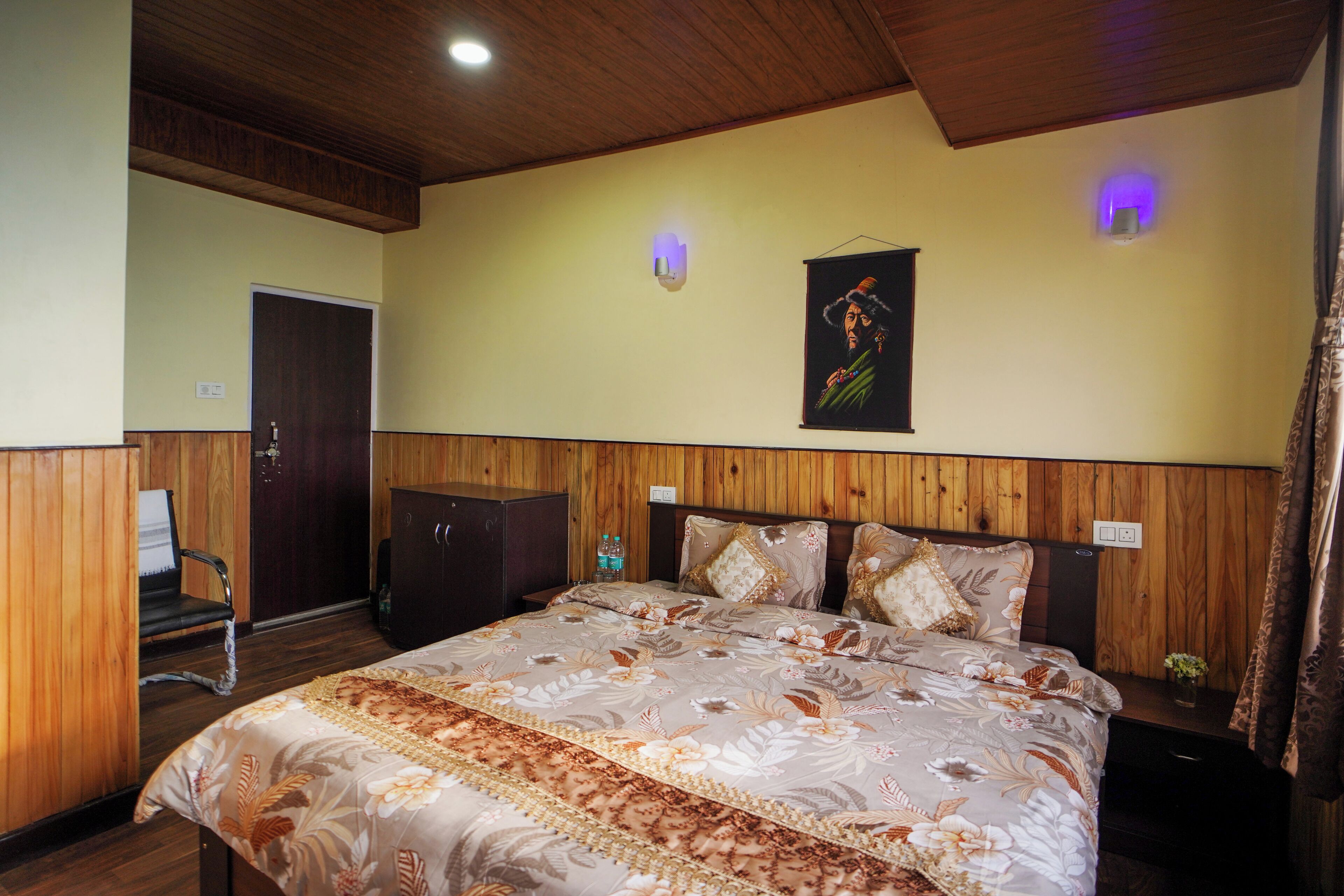 A bedroom with a wooden headboard, a bed with floral bedding, a nightstand, a chair, and a door.
