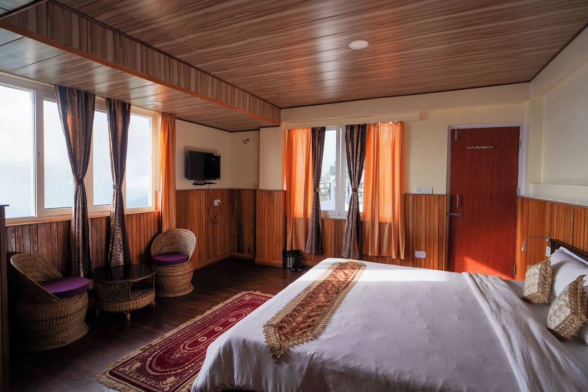 Een slaapkamer met een groot bed, houten wanden, een televisie en een raam met gordijnen.