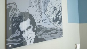 Een muur met een groot, monochroom kunstwerk waarop een persoon en abstracte vormen staan afgebeeld.