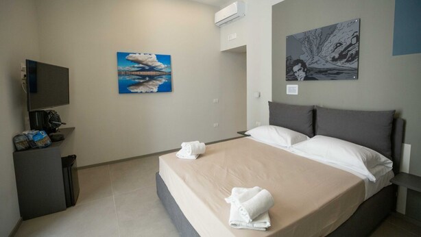 Een hotelkamer met een bed, een televisie, een schilderij en een prullenbak.