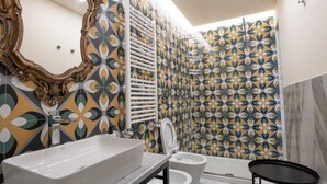 Une salle de bain avec un grand miroir, un lavabo blanc, deux toilettes et un espace douche.