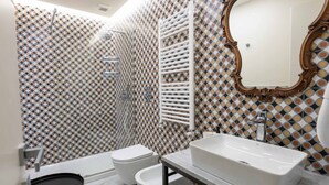 A bathroom with a patterned tile wall, a white bathtub, a toilet, and a sink with a mirror above it. - Ventaglieri 74 Majestic Room 2 By Dimorra (NAPOLI)