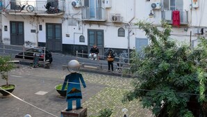 Escena urbana amb una estàtua, cotxes aparcats i edificis amb balcons.