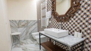 Un baño con piso de mármol, un lavamanos blanco, inodoro y un espejo con un marco decorativo.