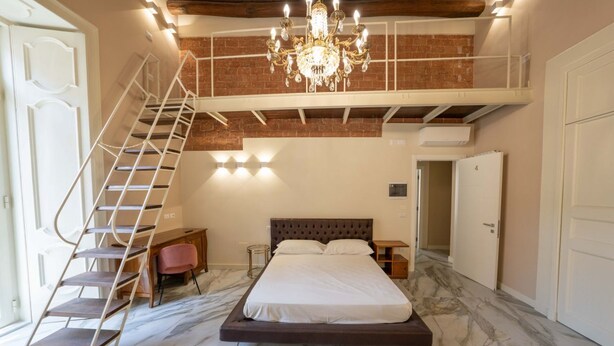 Un dormitorio con una cama grande, una escalera a un altillo superior, una araña y un suelo de mármol.